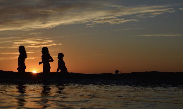 Silhouette of children running on beach at sunset.