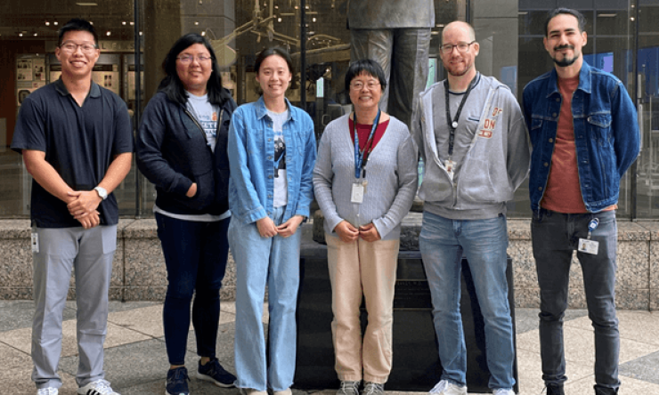 Six people smiling outside, in front of a bronze statue of Dr. Micheal E. DeBakey