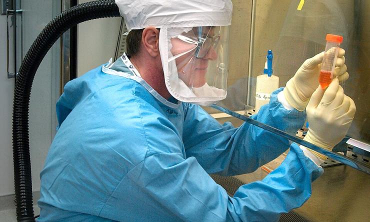 person in lab gear and lab headwear looking at a testing tube