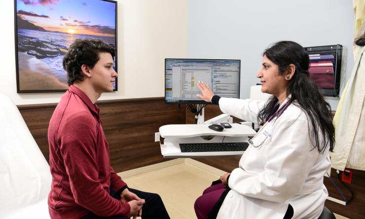 A doctor explaining information on a computer screen to a seated patient.