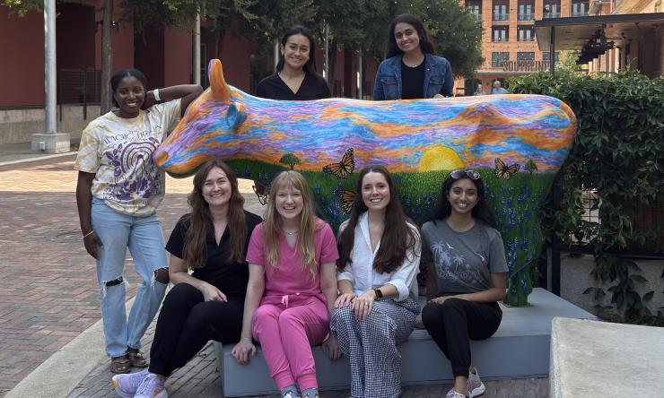 women standing with a painted cow sculpture, smiling