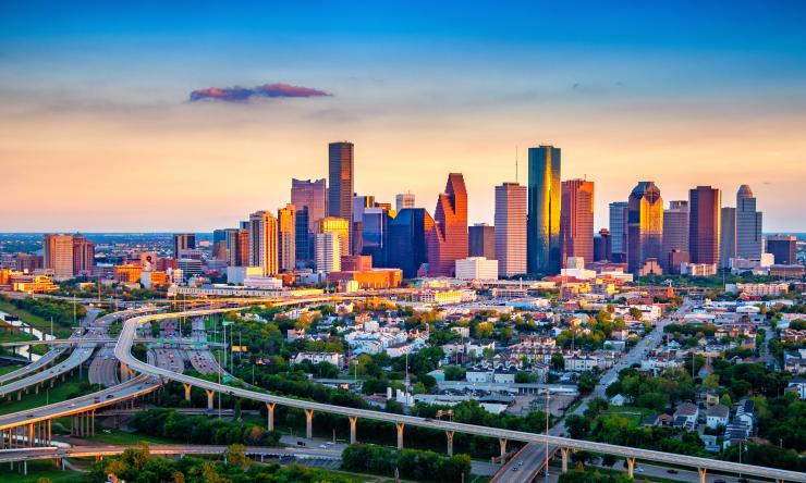 A colorful view of the Houston skyline, showing highways and tall buildings with the setting sun lighting up the city.