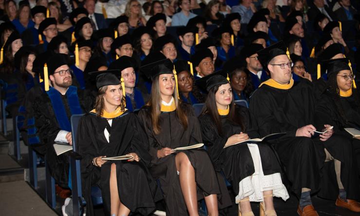 an auditorium of students at their graduation ceremony, dressed in black caps and gowns