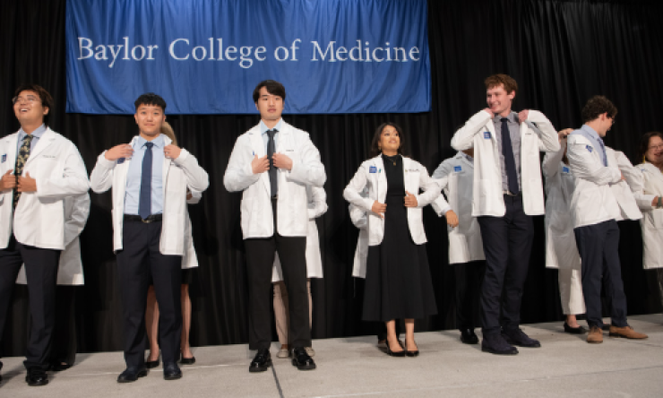 a group of people putting on their white doctor coat for the first time on a stage
