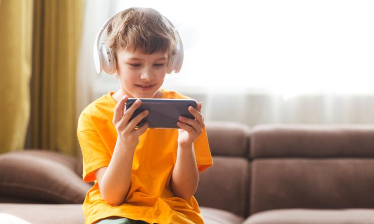 boy wearing headphones and a yellow shirt, looking at a phone screen