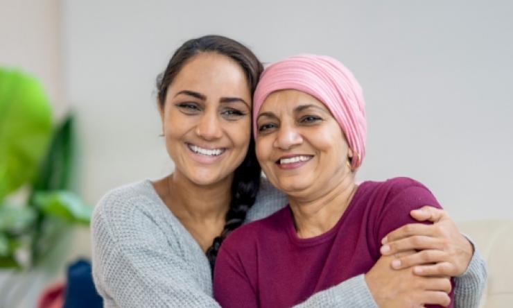 An adult daughter hugs her elderly mom who is wearing a head scarf to represent her battle with cancer.