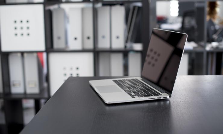 A photo of an open laptop on a table in a file room with full shelves behind the laptop. 