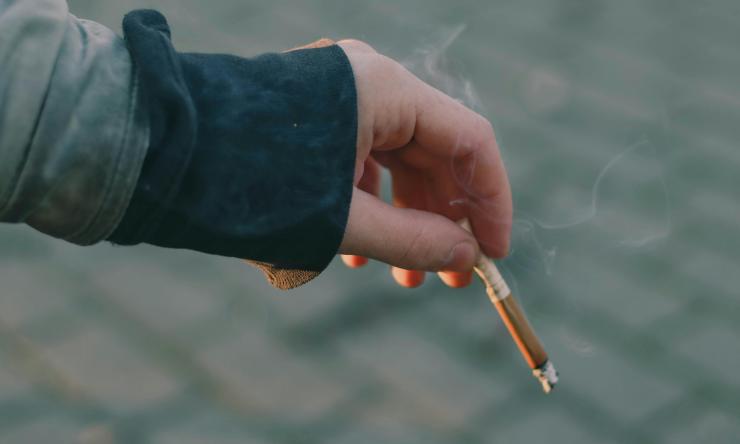 A close up photo of a hand holding a burning cigarette.