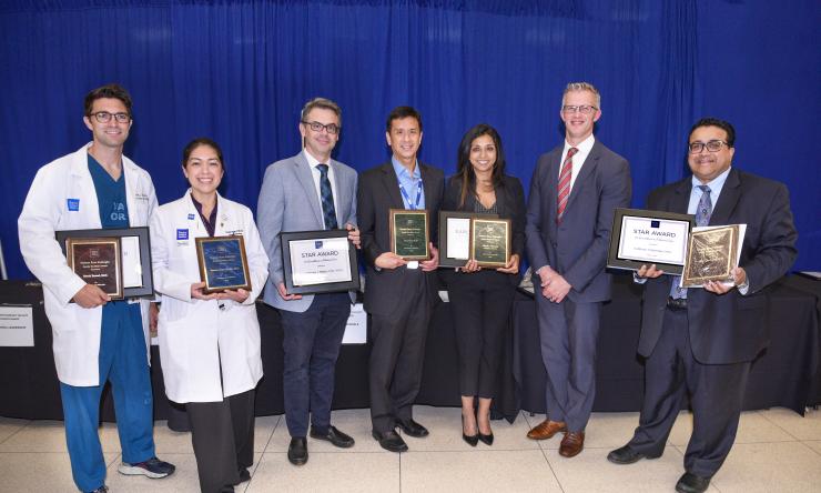 Six faculty members holding their award placards while smiling with a seventh person.