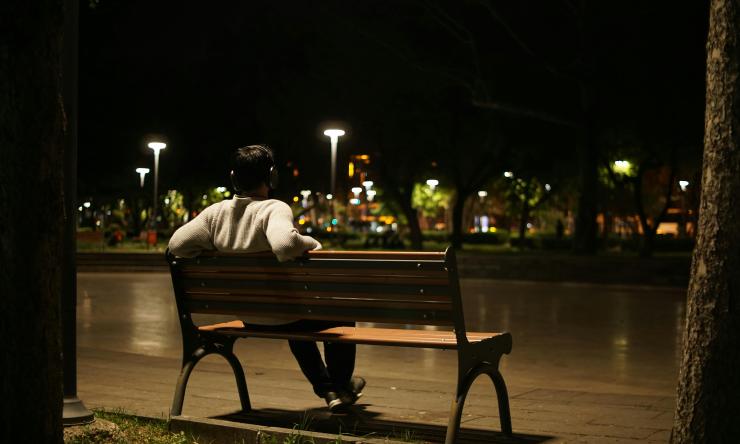 Photo of a man sitting on a bench overlooking a cityscape at night.