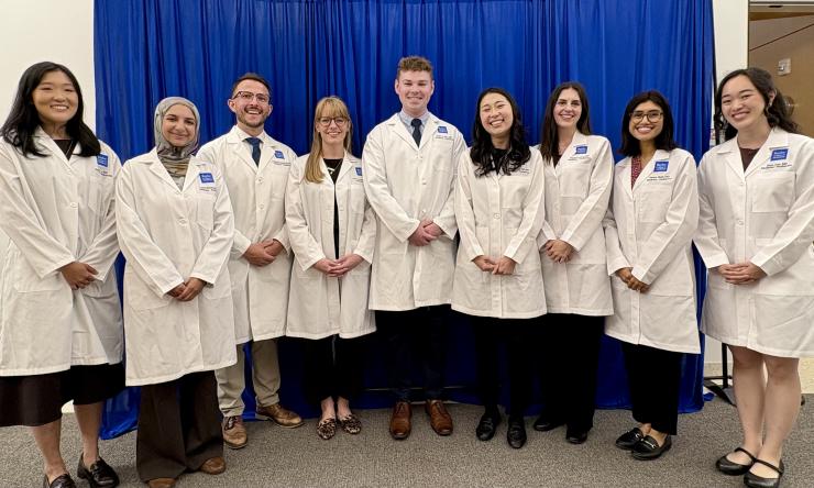Nine students in white coats lined up, smiling