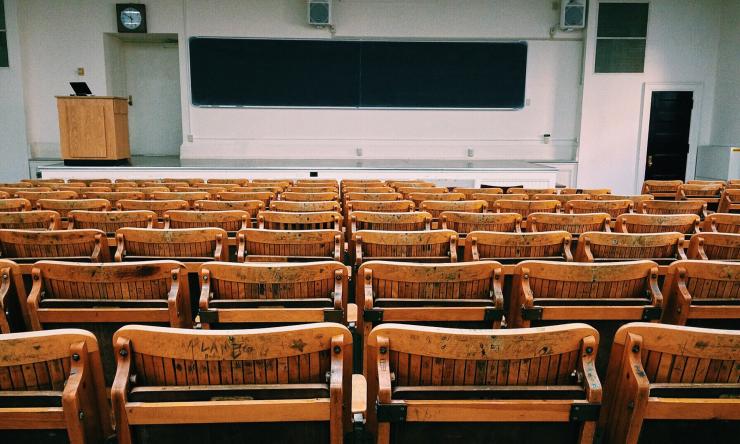 A photo of an empty college, auditorium style classroom with wooden chairs. 