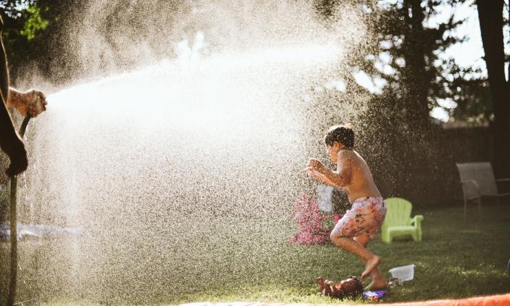 Photo of a child running through the spray of a water hose. 