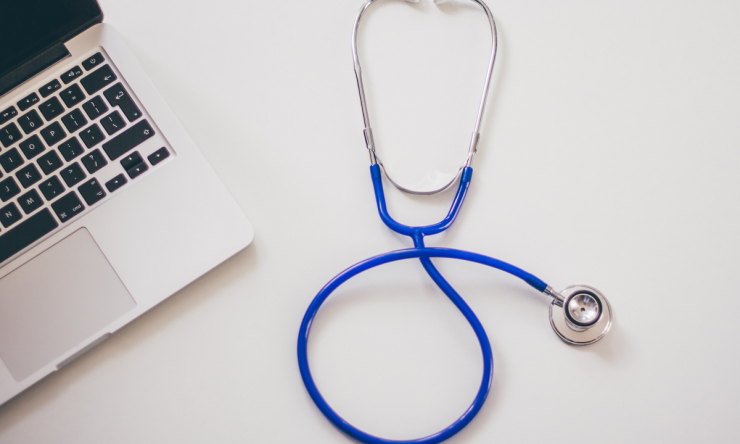 A photo of a doctor's desk including a laptop and a stethoscope.