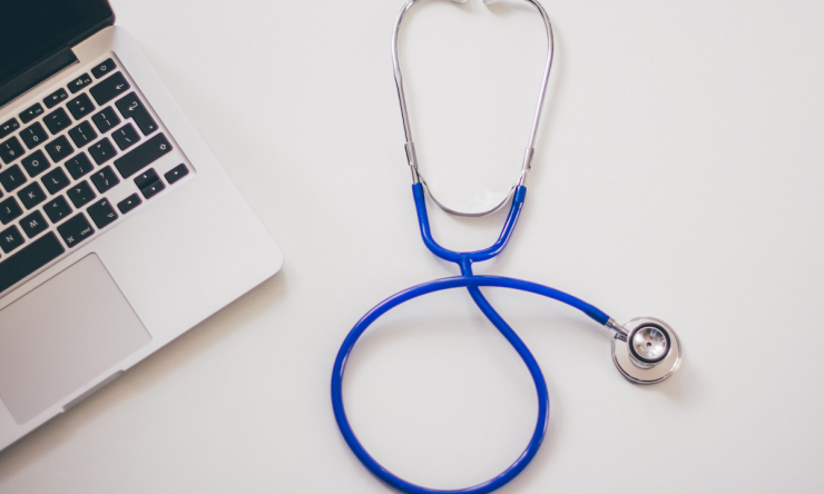 A photo of a doctor's desk including a laptop and a stethoscope.