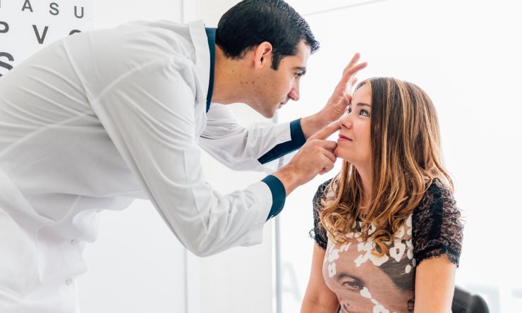 A patient sits while a doctor performs an eye exam.