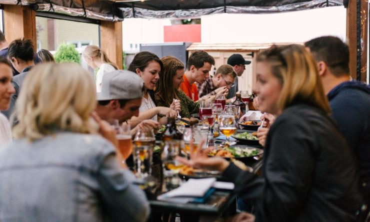 A group of friends enjoy a meal out together in a crowded restaurant.